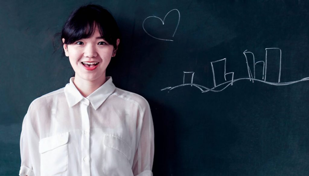 What are the 5 Hardest Languages to Learn, and Why? Photo of a smiling, Chinese teacher, standing in front of a blackboard.