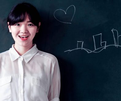 What are the 5 Hardest Languages to Learn, and Why? Photo of a smiling, Chinese teacher, standing in front of a blackboard.