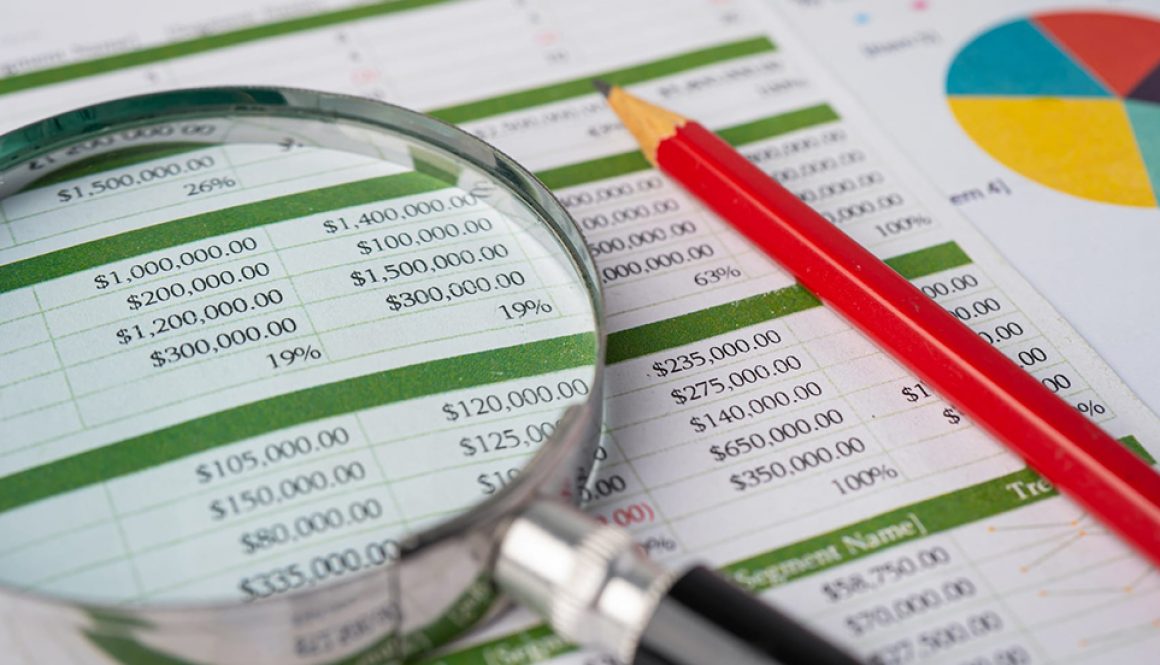 Magnifying glass with pencil on spreadsheet table and graph paper; about financial translations